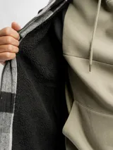 Sobrecamisa de corte recto con estampado de cuadros grandes en tonos gris y negro. Presenta cierre frontal con cremallera, cuello clásico, dos bolsillos frontales con solapa en el pecho y forro interior de sherpa para mayor calidez.