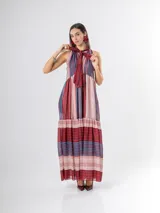 Vestido largo de corte halter en organdí, con estampado de rayas verticales y horizontales en tonos bordó, azul y crudo. Cuenta con un lazo en el cuello y un volado en la parte inferior.