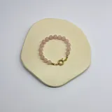 Pulsera elástica compuesta por cuentas esféricas de cuarzo rosa de 8 mm, unidas por nudos de hilo rosado.