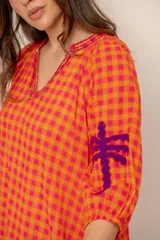 Vestido largo de corte holgado en tonos naranja y fucsia con estampado de cuadros vichy. Presenta cuello en V con detalles bordados, mangas tres cuartos y bordados decorativos de palmeras en contraste en las mangas.