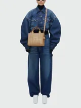 Cartera tipo tote de Marc Jacobs, confeccionada en cuero granulado negro. Presenta el logo de la marca estampado en el frente y doble asa superior.