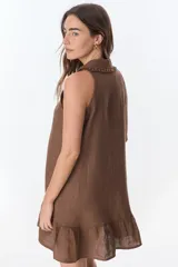Vestido corto sin mangas de lino, con cuello camisero, cierre frontal con botones y detalle de volado en el ruedo.