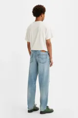 Jean de corte relajado y pierna cónica, con diseño de cinco bolsillos y cierre frontal con botones. Presenta un lavado azul claro con efecto desgastado, roturas localizadas y detalles de salpicaduras de pintura.