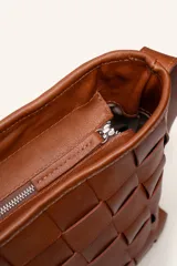Cartera tipo morral de cuero color beige, con diseño trenzado artesanal, correa larga regulable y cierre superior.