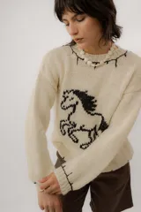 Buzo de punto color crudo, tejido a mano en 100% lana merino, con diseño de caballo en contraste y detalles de pespuntes negros en los bordes.