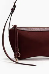 Cartera de hombro color borravino con acabado de textura suave, detalles en material sintético y cierre superior con tirador largo adornado con un nudo decorativo y argollas metálicas. Cuenta con una correa larga ajustable mediante hebilla.