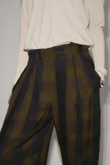 Pantalón de tiro alto con diseño fluido y estampado de cuadros en tonos oscuros. Presenta pliegues frontales, bolsillos delanteros con solapa y cierre frontal con cremallera, botón y ganchos metálicos.