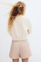 Short pollera de sarga color beige con diseño tableado, tira frontal con botones forrados decorativos y sutiles rayas finas.