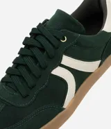 Championes de estilo retro tipo chuteira, color verde oscuro con detalles en blanco crema y suela de goma color caramelo. Presentan un acabado con efecto gamuza y cierre mediante cordones.
