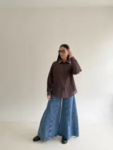 Camisa oversize de color marrón con cuello camisero y puños con detalle de bordado festoneado en color blanco. Presenta cierre frontal de botones y mangas largas.