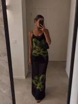 Vestido largo de microtul negro con estampado de flores grandes en tonos verdes. Presenta breteles finos, escote redondo y diseño ajustado al cuerpo con transparencias.