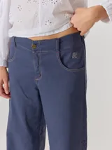 Pantalón tipo jean de corte relajado en color azul, con costuras en contraste y bordado decorativo en el bolsillo delantero. Presenta cierre con botón metálico y diseño de cinco bolsillos.