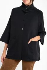 Cardigan negro de corte oversize, con cuello alto, cierre frontal de botones y mangas tres cuartos. Presenta un diseño holgado con bolsillos frontales y una caída fluida.
