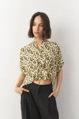 Blusa corta de manga corta con estampado en blanco y negro, cuello mao y cierre frontal con botones. Cuenta con detalle de elástico fruncido en la cintura que genera un efecto peplum.