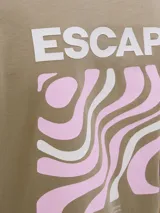 Remera color arena de manga corta y cuello redondo. Estampado en la espalda con la palabra 'ESCAPE' y un diseño abstracto en tonos rosa y blanco.