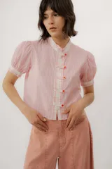 Blusa de diseño a rayas rosadas y blancas, con cuello mao, mangas cortas abullonadas, cierre frontal con botones tipo pastilla y detalles combinados en contraste.
