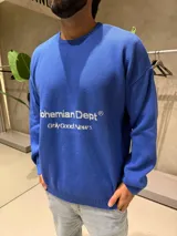 Sweater de tejido de punto color azul con cuello redondo y mangas largas. Presenta un estampado frontal en color blanco con el texto 'Bohemian Dept' y 'Only Good News'.
