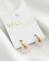 Aros de acero dorados con dije de acrílico en forma de flor color rosa pálido.