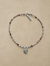 Gargantilla de cuentas de cristal multicolor con dije central de escudo metálico y placa identificatoria de la marca.