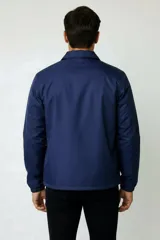 Campera estilo coach de poliéster color azul, con cuello camisero, cierre frontal con botones a presión y bolsillos laterales.