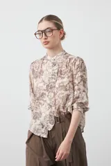 Camisa de manga larga con cuello con volados y botones nacarados. Presenta un estampado romántico de inspiración barroca en tonos azul y beige.