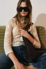 Blusa de manga larga color crema, con cuello alto y detalles de encaje y bordados florales. Presenta paneles verticales con entredoses y un tejido semitransparente.