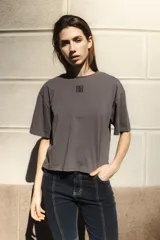 Remera blanca de algodón con corte boxy y cuello redondo. Presenta un pequeño logo bordado en color cobre en el centro del pecho.