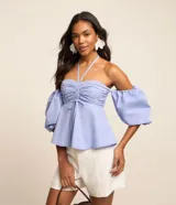 Blusa de tricolina color celeste, con diseño hombro a hombro, escote halter, fruncido en el pecho con lazo ajustable, y mangas abullonadas cortas.