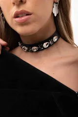 Gargantilla tipo choker de cuero sintético negro, decorada con una hilera de cristales facetados en diferentes formas y tamaños. Cuenta con cierre ajustable mediante cadena de acero quirúrgico.
