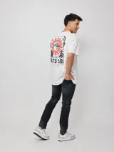 Remera blanca de algodón con estampado en la espalda que incluye un sol con un surfista en el centro, texto y motivos playeros.