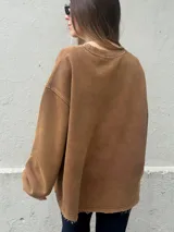 Buzo oversize de color negro con calce relajado y mangas amplias. Presenta letras en relieve con bordes desflecados en el frente y un ruedo inferior también desflecado.