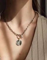 Collar de cadena de eslabones alargados con cierre frontal tipo T y dije circular de textura rústica e irregular.