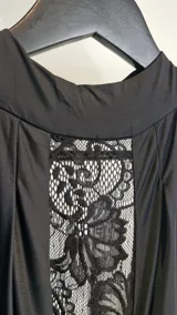 Vestido largo de fiesta color negro, con cuello halter alto y detalle de panel frontal de encaje transparente. Presenta diseño drapeado en el escote y la cintura, corte ajustado al cuerpo y espalda descubierta.