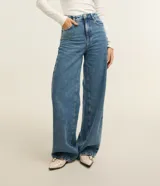Pantalón wide leg de denim azul de talle alto con costuras pespunteadas en contraste. Cuenta con trabillas en la cintura, cierre de botón y cremallera, y bolsillos delanteros y traseros.