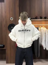 Buzo con cierre frontal completo, capucha amplia y bolsillos tipo canguro. Presenta estampado gráfico en el pecho con la marca IttaiStars y diseño de corte holgado.