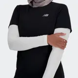 Remera deportiva New Balance de manga corta, color negro, con logo NB plateado en el pecho. La modelo la combina con mangas largas blancas debajo y calzas negras.