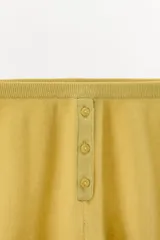 Shorts de tejido de punto color mostaza, de tiro alto con cintura elástica y detalle de botones frontales a tono.