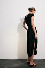 Vestido midi color negro de escote en V y manga corta, con detalle de fajín drapeado cruzado en la cintura y falda abullonada de corte asimétrico.
