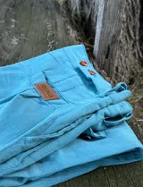 Pantalón de vestir de tusor color verde petróleo, con cintura alta, cierre frontal con botones marrones y lazo de tela para ajustar. Incluye un parche de cuero marrón con el logo "MILONGA" en el área de la cintura.