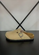 Zuecos de gamuza color beige con hebilla metálica lateral ajustable y suela de corcho con base de goma negra.