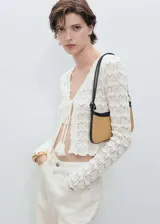 Cardigan de crochet color blanco, con cuello en V, manga larga y cierre frontal mediante lazos con borlas. Presenta un diseño calado con textura.