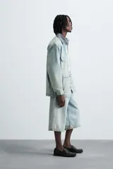 Bermudas de denim de algodón, color celeste claro con efecto lavado y manchas marrones/beige en las perneras. Tienen un corte ancho (baggy fit) y terminación de bajo irregular.