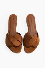 Sandalias planas de gamuza color marrón tostado, con punta almendrada y una tira ancha trenzada en el empeine. Cuentan con plantilla de cuero y bordes ribeteados en color negro.