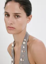 Top gris de corte entallado y escote halter, sin mangas, confeccionado en mezcla de lino y algodón. Presenta un diseño adornado con botones decorativos de nácar a lo largo del escote y los tirantes.