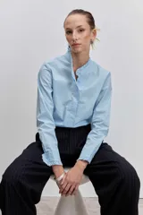 Camisa de algodón color celeste, con cuello mao y puños con detalle de volados. Presenta cierre frontal oculto con botones y un diseño de corte clásico.