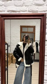 Campera estilo gamulán de cuero sintético negro con interior y solapas de corderito blanco. Presenta cierre frontal, bolsillos laterales y cinturón ajustable en el ruedo.