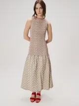 Vestido midi sin mangas de silueta en A y escote redondo, confeccionado en algodón. Presenta cuerpo superior con fruncido elástico y estampado geométrico, y falda evasé con diseño estampado de ondas y ruedo festoneado en tono rojo.