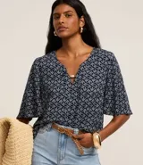 Blusa tipo bata de mangas cortas, confeccionada en viscosa con estampado de follaje en blanco sobre fondo azul marino. Tiene escote en V con detalle de abalorio en el centro.