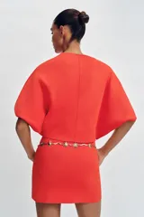 Top corto de punto color rojo coral, con cuello redondo y mangas cortas amplias con sisa ancha y costura central vertical.