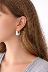 Aros tipo argolla de diseño semicircular, combinando una estructura metálica con baño de oro y una pieza de acrílico blanco de alta calidad.